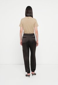 Beige cotton t-shirt with short sleeves, paired with dark satin joggers featuring an elastic waistband and side pockets, viewed from the back.