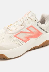 Baskets légères en crème avec des accents roses, tige en mesh, semelle en caoutchouc texturée, embout renforcé et logo 'N' bien visible sur les côtés.