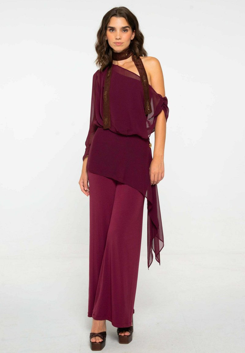 Conjunto de dos piezas burdeos con un top drapeado que presenta mangas transparentes y un detalle de gargantilla, combinado con pantalones de pierna ancha y tacones de plataforma.