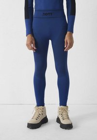 Blauwe sportleggings met getextureerde strepen en een zwarte tailleband met het logo "ZOTT." Gecombineerd met beige wandelschoenen.