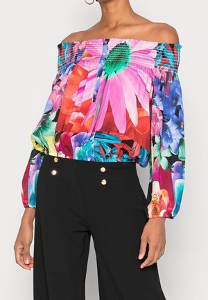 Off-shoulder blouse with vibrant multicolored floral print, smocked neckline, button front, and long puffed sleeves paired with black pants.