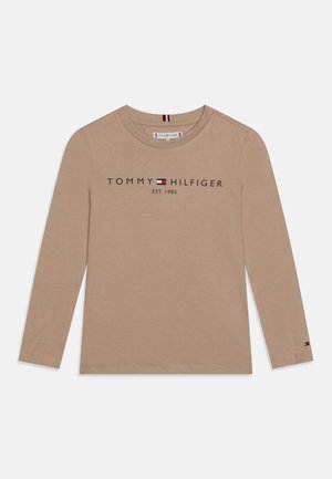 Beżowa koszula z długim rękawem i okrągłym dekoltem, z napisem "Tommy Hilfiger EST. 1985" i logo na piersi oraz małym logo na mankiecie lewej rękawa.