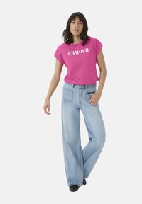 Pink short-sleeve t-shirt with "L'AMOUR" text in white, paired with light blue wide-leg jeans. Smooth fabric, relaxed fit, basic design.