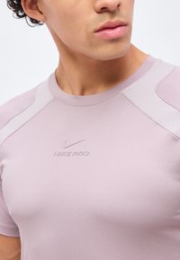 Gros plan d'une personne portant un t-shirt de sport Nike Pro violet clair avec des panneaux en mesh aux épaules et un petit logo swoosh sur la poitrine.