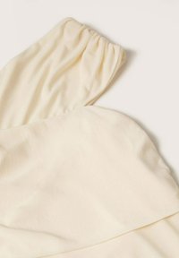 Tissu en coton de couleur crème avec un poignet élastique froncé, probablement une partie d'une manche, sur un fond blanc uni.