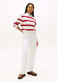 Rød og hvidstribet sweatshirt med "Tommy Hilfiger"-logo, parret med hvide brede bukser og brune loafers. Glatte teksturer hele vejen igennem.