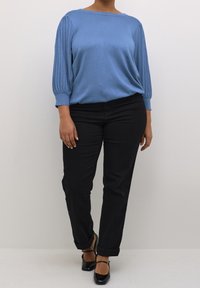 Pull bleu clair avec manches plissées, associé à un pantalon noir droit et des chaussures noires et marron. Texture douce, coupe décontractée.
