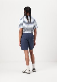 Stribet t-shirt med korte ærmer, blå og hvidt mønster, kombineret med marineblå shorts med elastisk talje og to baglommer.