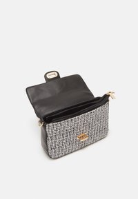 Petit sac à main rectangulaire avec rabat en cuir noir, devant tissé en noir et blanc, fermoir doré et compartiment intérieur zippé, montré ouvert.