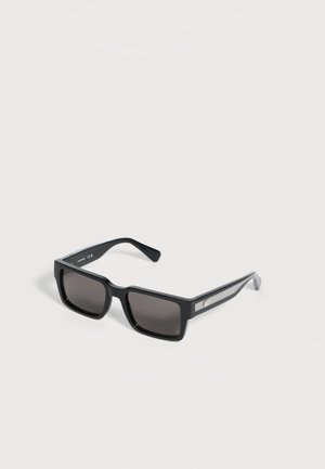 Lunettes de soleil rectangulaires noires avec des verres teintés foncés et des branches texturées avec un petit logo métallique sur le côté.