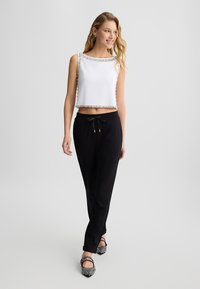 Top crop bianco con rifiniture di gioielli, abbinato a pantaloni jogger neri con coulisse e scarpe con motivo bianco e nero. Tessuti lisci in tutto.