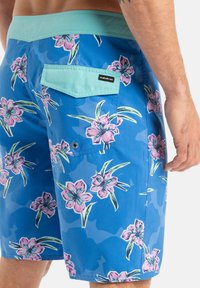 Blå simshorts med blommönster som har rosa blommor och gröna blad. Tillverkade av lätt material med en mintgrön midja och bakficka.
