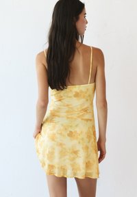 Gelbes Blumendruckkleid mit dünnen Trägern und lockerer Passform, das eine weiche, transparente Textur und einen leicht ausgestellten Saum hat.