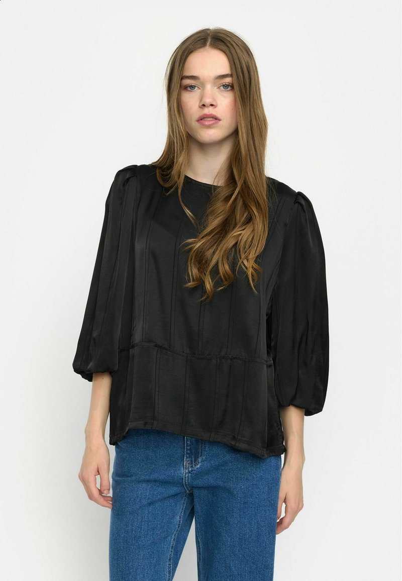 Top in satin nero con maniche a sbuffo, caratterizzato da cuciture verticali, scollatura rotonda e vestibilità ampia, abbinato a jeans in denim blu.