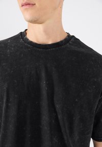 Tricou negru cu mânecă scurtă, realizat dintr-un material moale și texturat, având un guler rotund și un finisaj ușor decolorat.