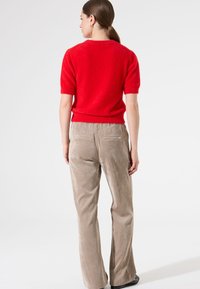 Roter, flauschiger, kurzärmeliger Pullover kombiniert mit hellbeigen, karierten weit geschnittenen Hosen. Das Outfit hat eine lockere Passform und eine weiche Textur.