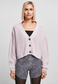 Lys lavendelfarget, cropped cardigan i strukturert strikk, dyp V-hals og tre svarte knappdetaljer, iført over mønstrede svarte leggings.