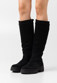 Botas negras de ante hasta la rodilla con suela gruesa, cierre lateral, textura suave y un sutil detalle de costura.