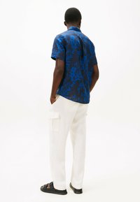 Camicia a maniche corte, di colore blu navy con un motivo floreale blu, abbinata a pantaloni cargo color crema e sandali neri. Tessuto morbido, vestibilità rilassata.