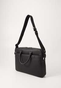 Sac fourre-tout noir avec une finition texturée, poignées supérieures doubles et une bandoulière réglable. Doté d'une fermeture zippée et d'accents minimalistes.