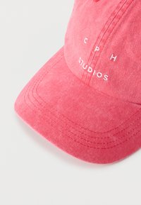 Ροζ βαμβακερό καπέλο μπέιζμπολ με κυρτή γείσο και λευκή κεντητή επιγραφή "CPH STUDIOS" στην μπροστινή πλευρά, σε λευκό φόντο.
