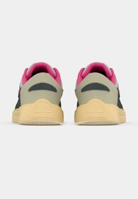 Dunkelgrüne und beige Sneakers haben einen rosa Kragen und eine Innensohle, kombiniert mit einer strukturierten gelben Gummisohle und einem Logoschriftzug auf der Ferse.