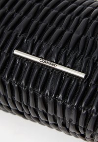 Svart lær clutch med teksturert, quiltet design. Har en sølvfarget metallstang med "Calvin Klein" gravert som et merkevareelement.