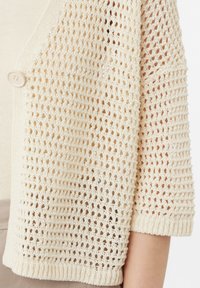 Strickjacke in Off-White mit offener Webstruktur, kurzen Ärmeln und einem Knopfverschluss. Weiches, leichtes Material.