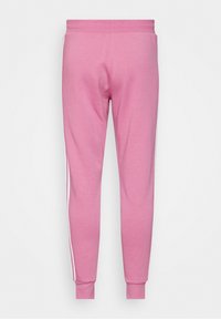 Różowe bawełniane spodnie dresowe o dopasowanym kroju, z białymi paseczkami po bokach i elastycznymi mankietami. Materiał ma gładką fakturę i miękkie wykończenie.