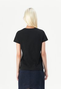 Black cotton t-shirt with short sleeves and a round neckline, worn with a textured navy skirt. Clean, simple design.