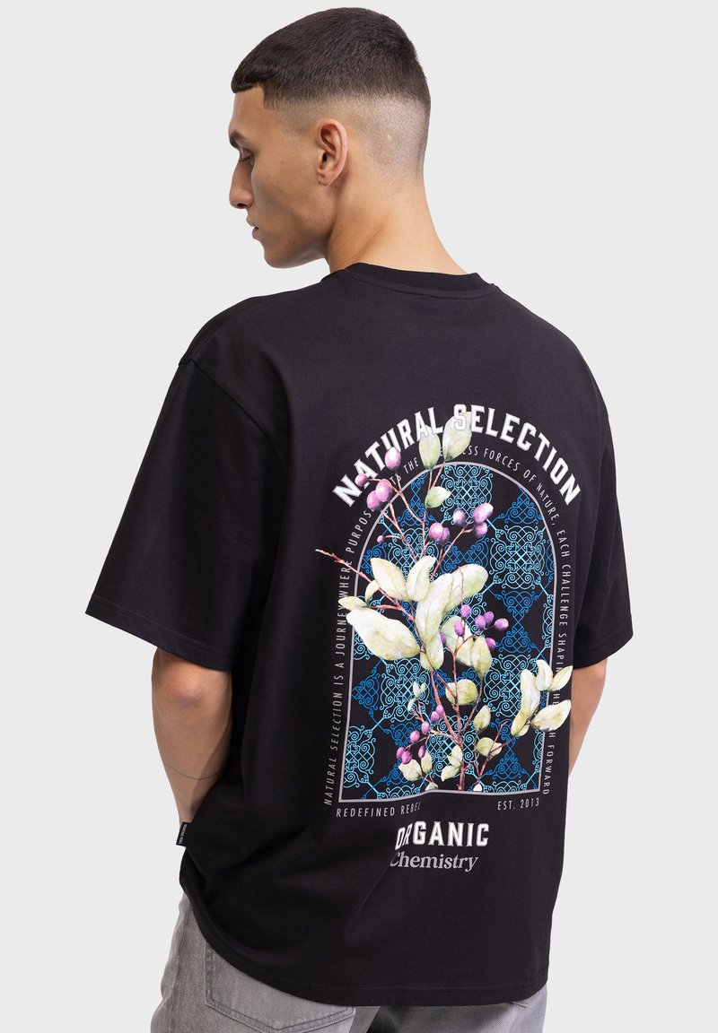 Schwarzes, oversize T-Shirt mit floralem Grafikdesign in Weiß, Blau und Pink auf der Rückseite, mit Textangaben "Natürliche Selektion" und "Organische Chemie."