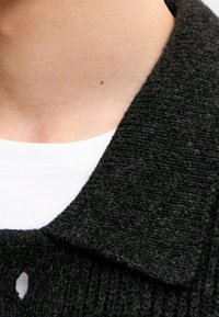 Charcoal gray knitted collar with a textured finish, layered over a white crew neck shirt. Button detail visible at the neck.