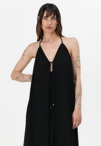 Musta halterneck-mekko, jossa on syvä V-pääntie ja etupuolella solmittava yksityiskohta. Kevyestä kankaasta valmistettu malli, jossa on säädettävät olkaimet ja virtaava siluetti.