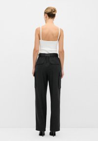 Zwarte high-waisted cargobroeken met zijzakken, gecombineerd met een witte mouwloze top. Gladde textuur, wijduitlopende pasvorm en verborgen tailleband.