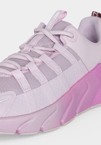 Ανοιχτόροζ αθλητικό παπούτσι Nike Free με υφασμάτινο επάνω μέρος, επενδεδυμένο κολάρο, κορδόνια με θηλιές και παχύ, υφή, σόλα που μεταβαίνει από ανοιχτό σε πιο σκουρόροζ.