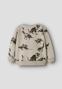 Sweat-shirt beige avec des impressions de dinosaures noirs dans diverses poses. Poignets et ourlet côtelés, col rond, et texture de tissu douce.