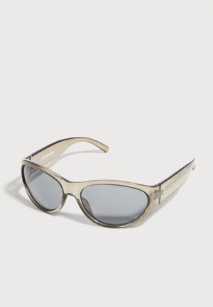 Ochelari de soare stil cat-eye bej transparent cu lentile închise la culoare așezați pe o suprafață albă.