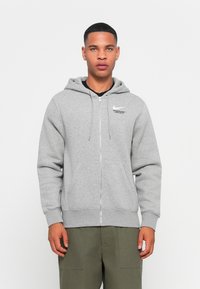 Grijze zip-up hoodie gemaakt van zachte stof, met een trekkoord capuchon, kangoeroezakken en een Nike-logo op de linkerborst.