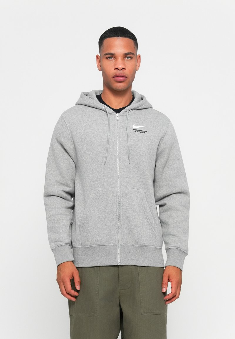 Grijze zip-up hoodie gemaakt van zachte stof, met een trekkoord capuchon, kangoeroezakken en een Nike-logo op de linkerborst.