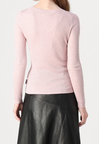 Top moulant à manches longues de couleur rose clair avec un design ajusté. Texture douce, encolure ronde et une étiquette sur le côté gauche près de la taille.