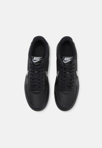 Paire de baskets Nike noires avec logos swoosh blancs et lacets noirs, vues de dessus sur un fond blanc.
