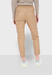 Béžové kožené kalhoty s elastickým pasem, slim fit a dvěma zadními kapsami. Hladká textura a zúžený design nohavic.