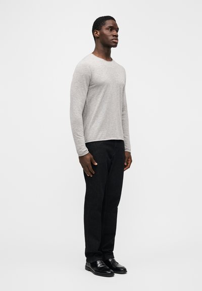 Ανοιχτό γκρι μακρυμάνικο πουκάμισο με στρογγυλή λαιμόκοψη, απαλή υφή, σε συνδυασμό με μαύρο τζιν ίσιας γραμμής και μαύρα παπούτσια, στέκεται μπροστά σε απλό φόντο.