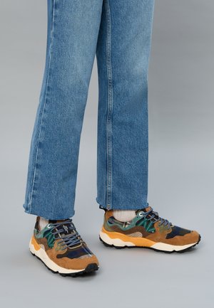 Scarpe da ginnastica multicolori con pelle scamosciata marrone, dettagli verdi e tomaia in tessuto a fantasia. Suola in gomma e design con lacci. Indossate con jeans blu.
