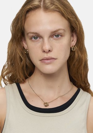 Goldfarbene Halskette mit ineinandergreifenden kreisförmigen Anhängern und einer strukturierten Kette. Modell trägt passende goldfarbene Creolen. Neutraler Tanktop.