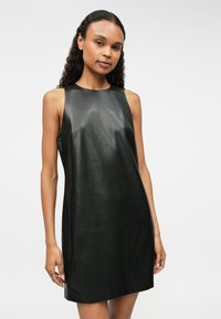 Μαύρο αμάνικο δερμάτινο φόρεμα με απλή υφή και ευθεία γραμμή. Διαθέτει στρογγυλή λαιμόκοψη και ελαφρές πλαϊνές σχισμές για ευκολία κίνησης.
