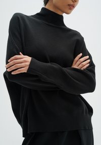 Pulover negru cu guler înalt tricotat, cu un croi supradimensionat, mâneci lungi și un decolteu cu textură fină.