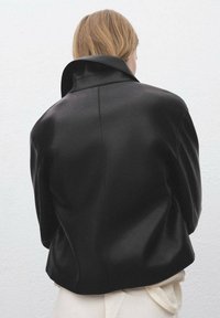 Čierna kožená bunda s širokým golierom, so štruktúrovanými plecami a uvoľneným strihom. Hladká textura a minimalistické detaily dizajnu.