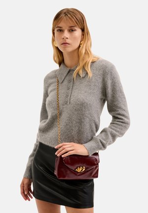 Šedý svetr z vlněné směsi s límečkem a předními knoflíky, kombinovaný s černou koženou mini sukní a texturovanou vínovou kabelkou se zlatými akcenty.