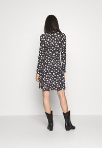 Svart klänning med långa ärmar, med ett rosa hjärtmönster och vita prickar, som vidgar sig något vid fållen. Bärs med svarta klackboots.